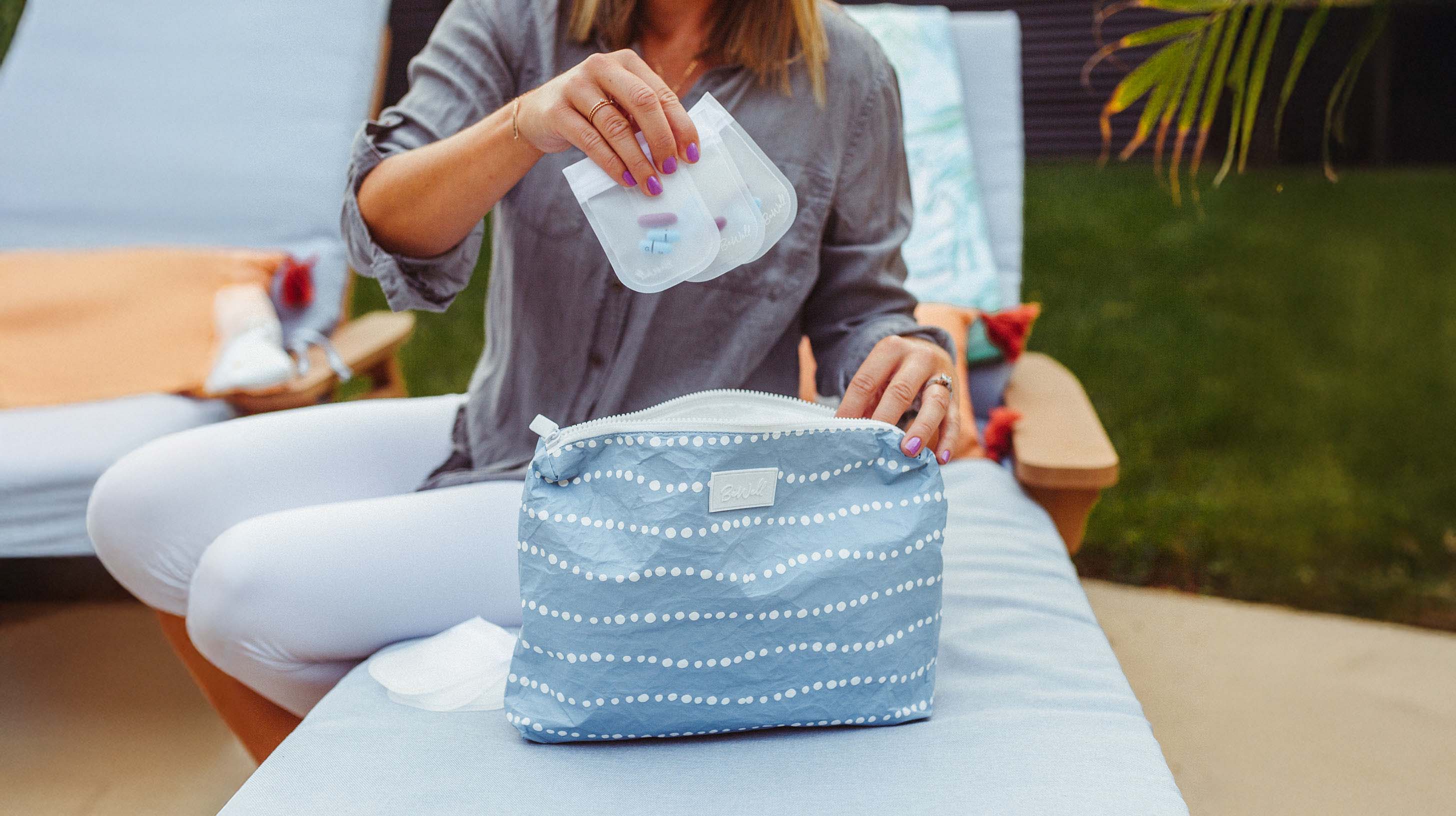Woman demonstrating a blue patterned pill pouch by holding open its lid to display interior storage capacity.