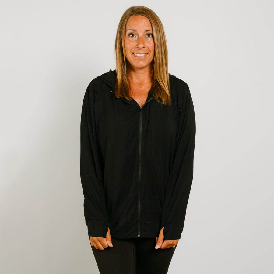 Woman wearing a black zip-up hoodie with orange accent cuffs against a white background.