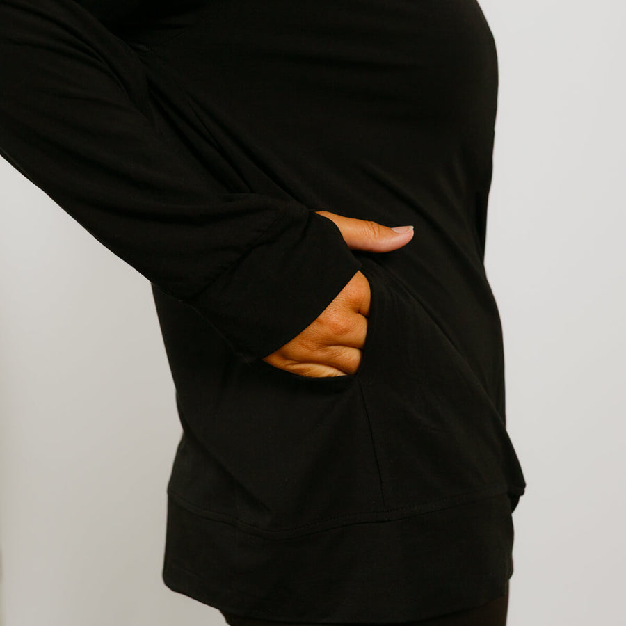 Black zip hoodie displaying open side zipper pockets with person's hand visible through opening.