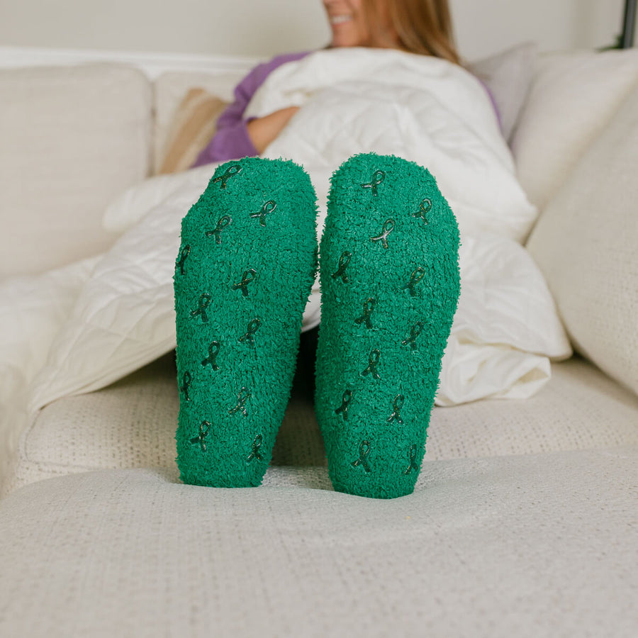 Close-up of green Rest Day socks with small pattern detail, worn by person lying on couch.