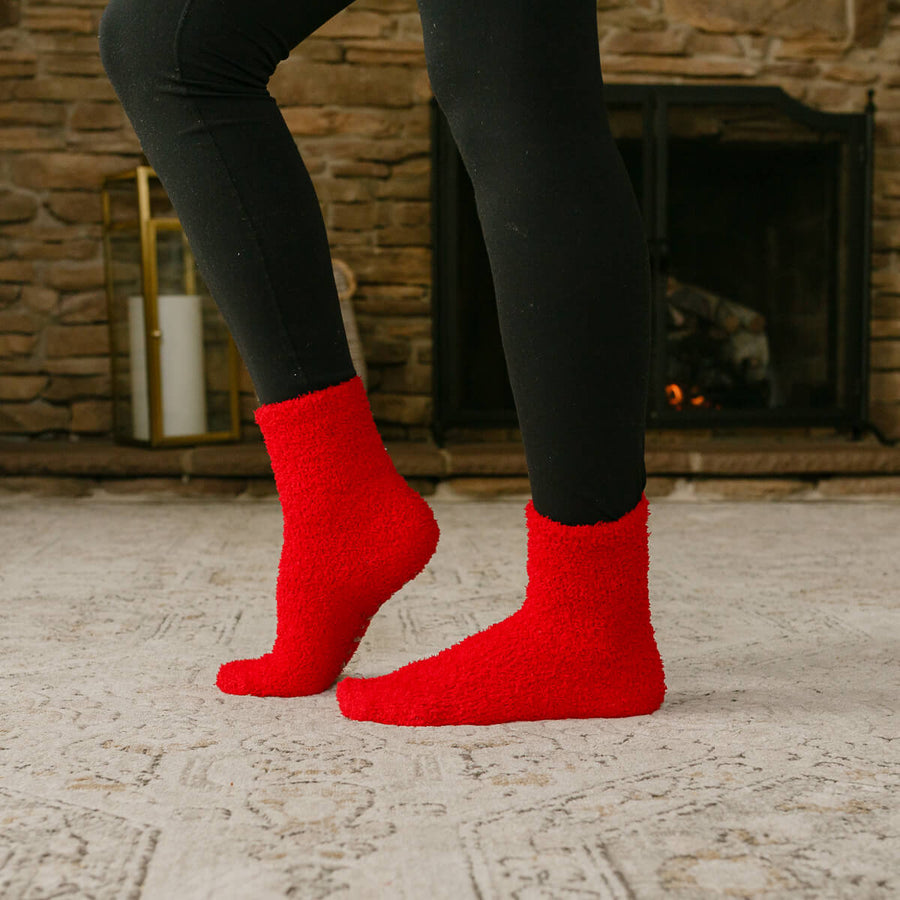 Person wearing red Rest Day socks with black leggings, standing indoors by fireplace.