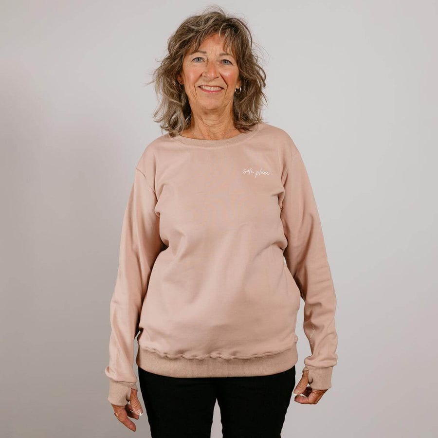 Woman wearing a beige crewneck sweatshirt with black pants against a white background.
