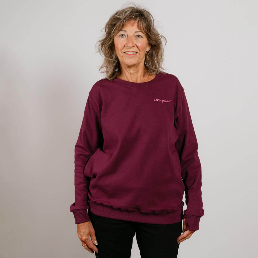 Woman wearing a burgundy crewneck sweatshirt with small text on chest, standing against neutral background.