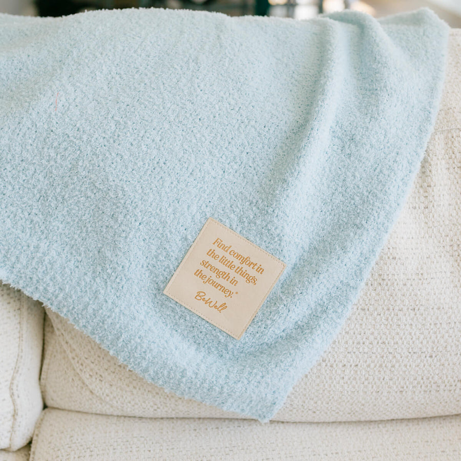 Light blue infusion day blanket draped over cream chair with tan product label visible.