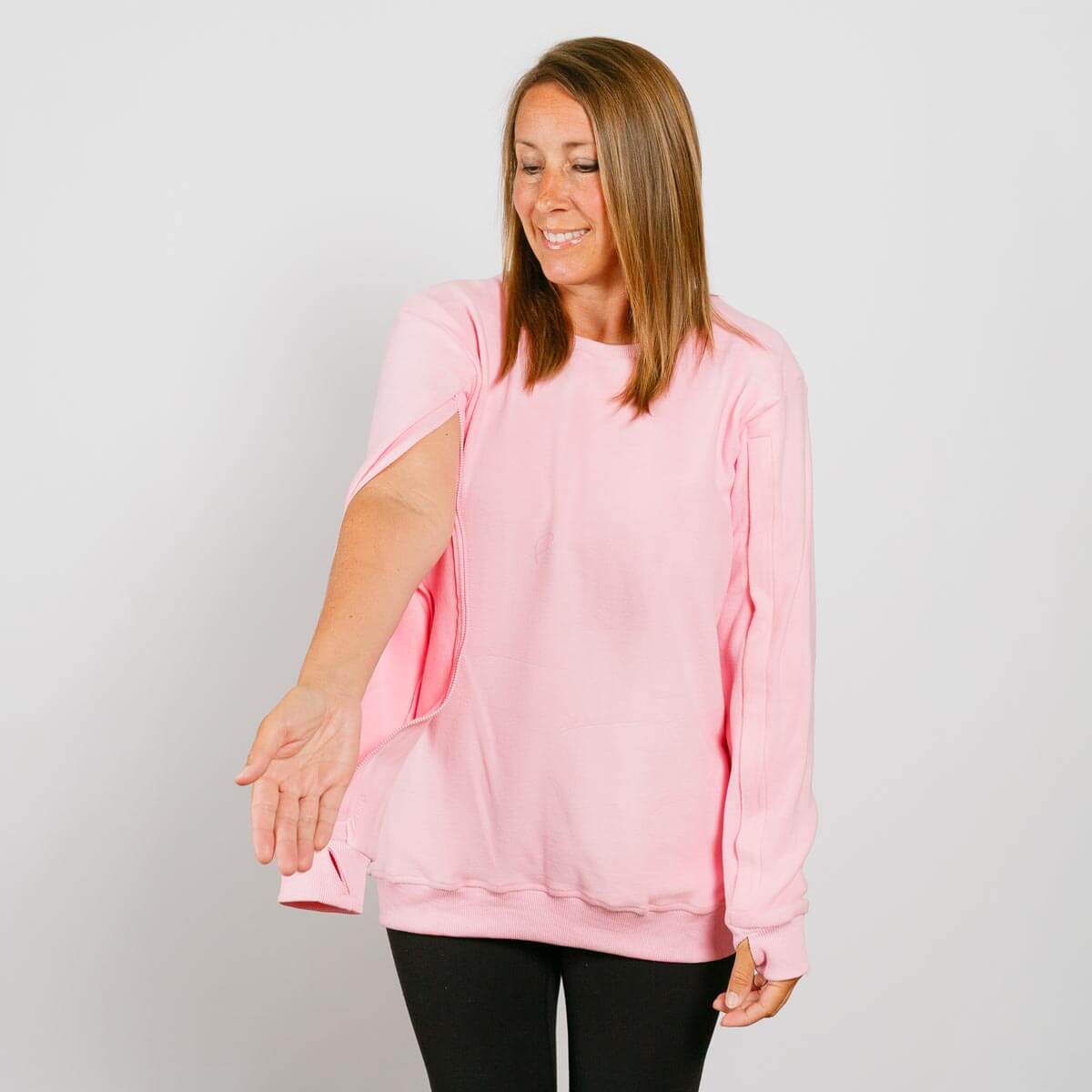 Woman wearing a pink crewneck sweatshirt over black pants, smiling while looking down.