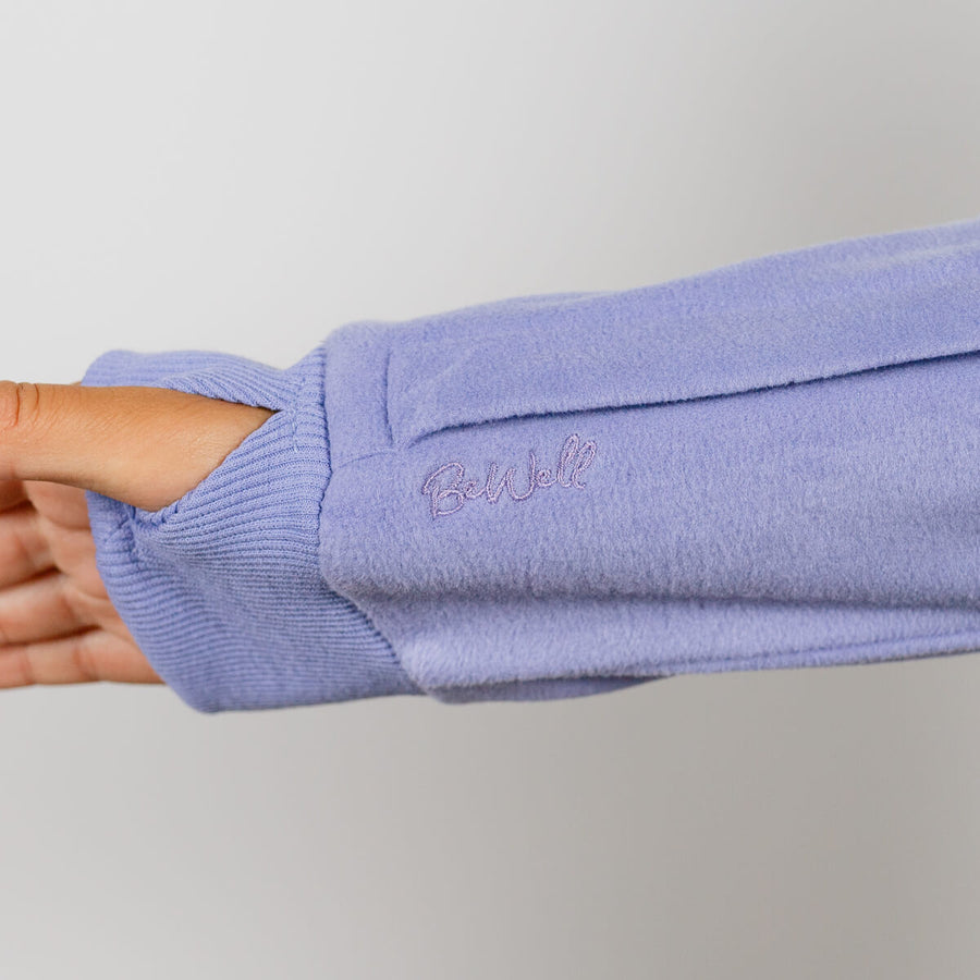 Person wearing a light purple crewneck sweatshirt with ribbed cuffs and collar detail.
