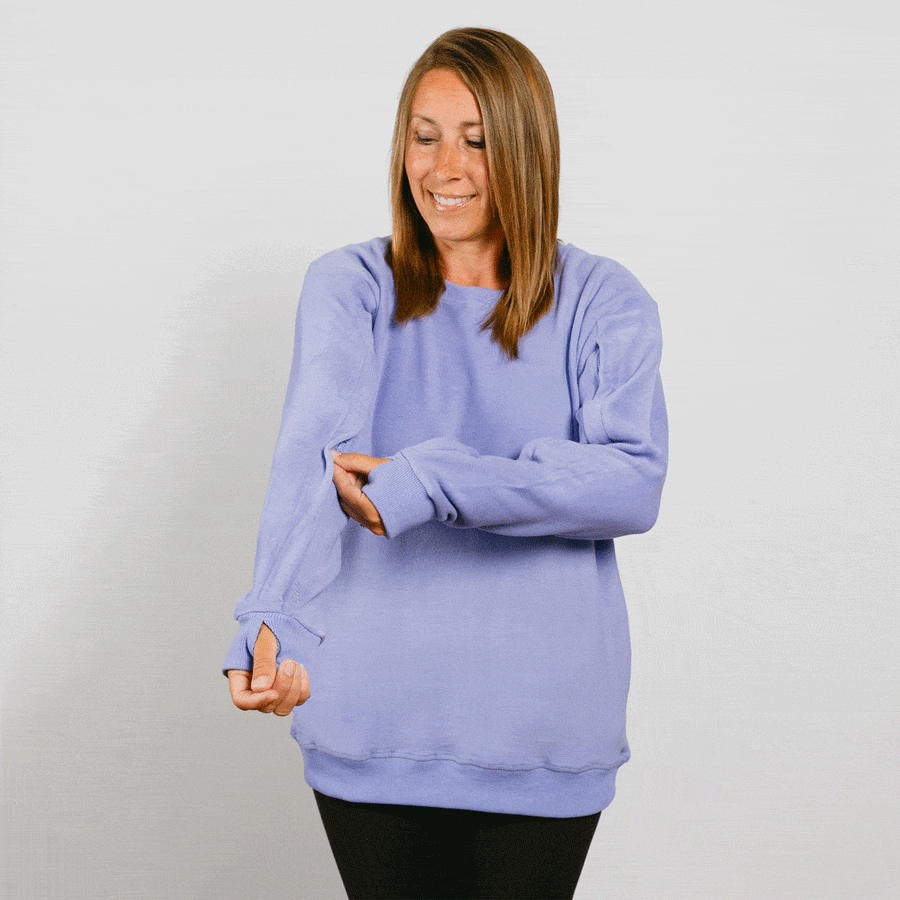 Pregnant woman wearing a light purple crewneck sweatshirt over black pants, smiling downward.