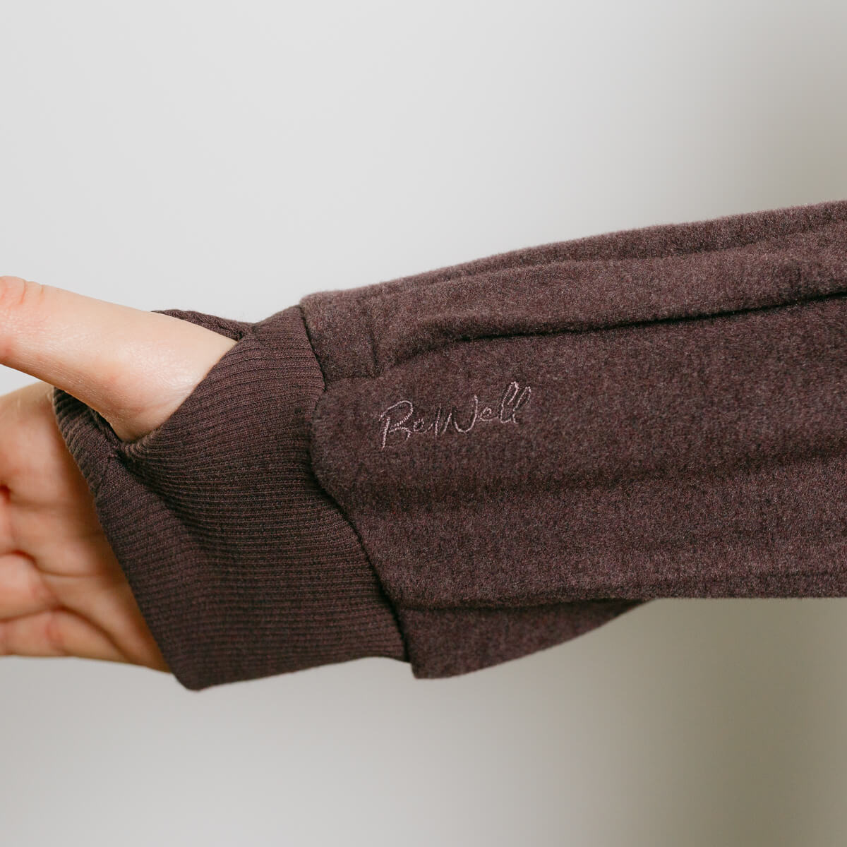 Person wearing brown IV crewneck with visible left arm access zipper detail.
