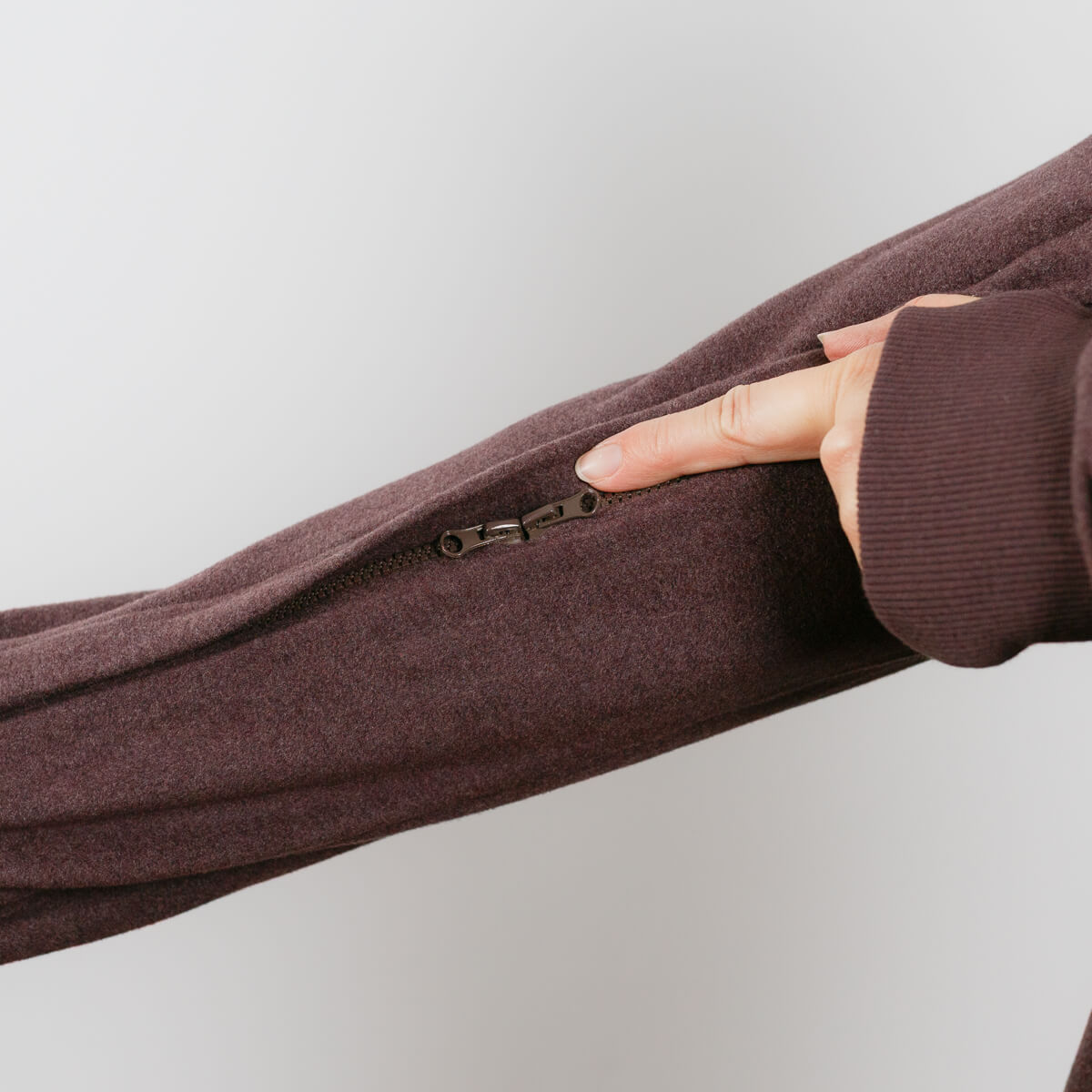 Person wearing brown IV crewneck with visible left arm access zipper detail.