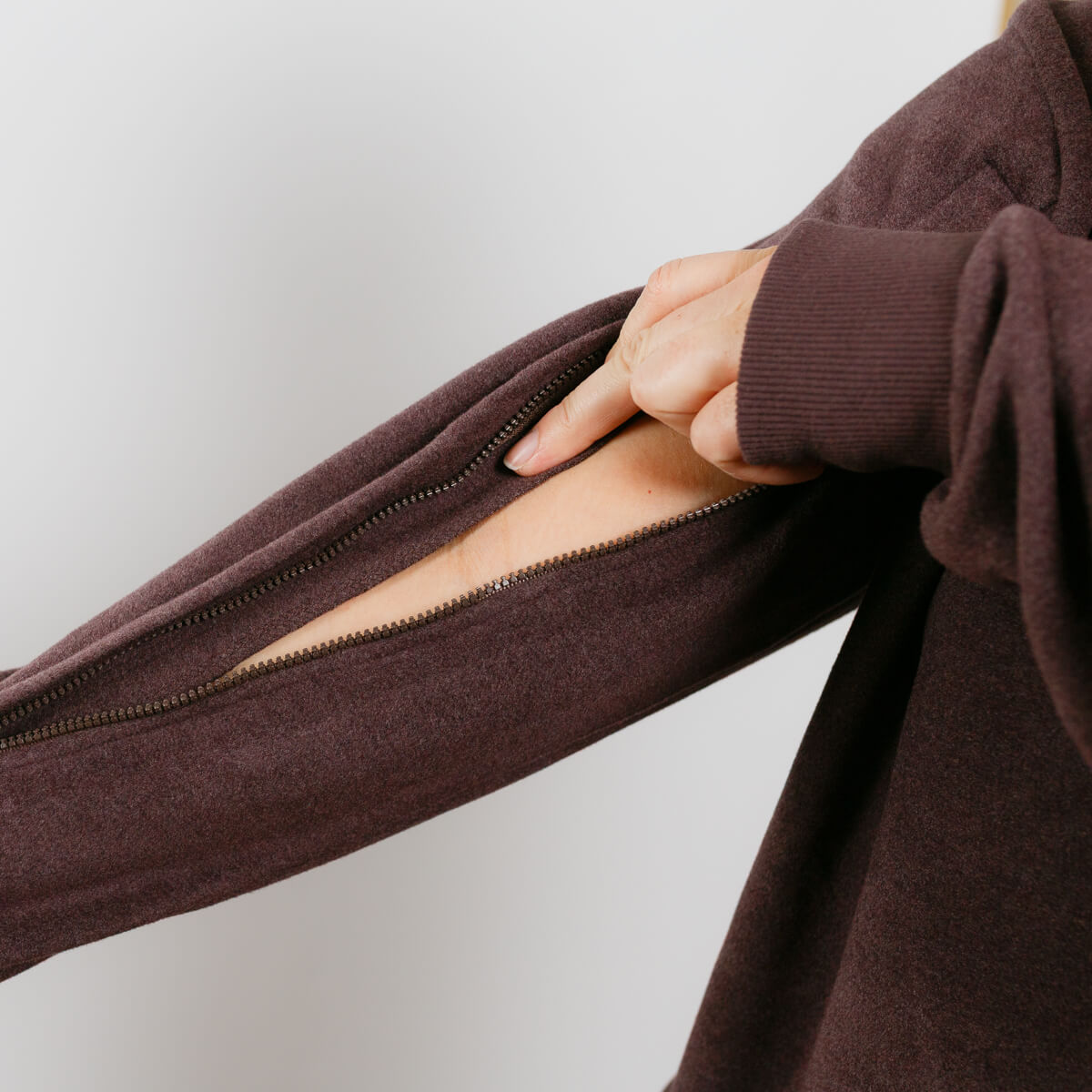 Person wearing brown IV crewneck, demonstrating open arm zipper access detail.