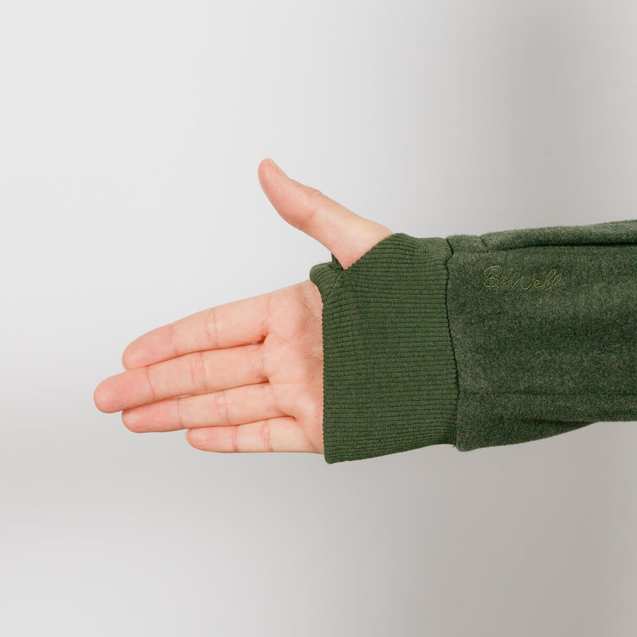 Person wearing olive green IV crewneck with arm extended showing ribbed cuff detail.