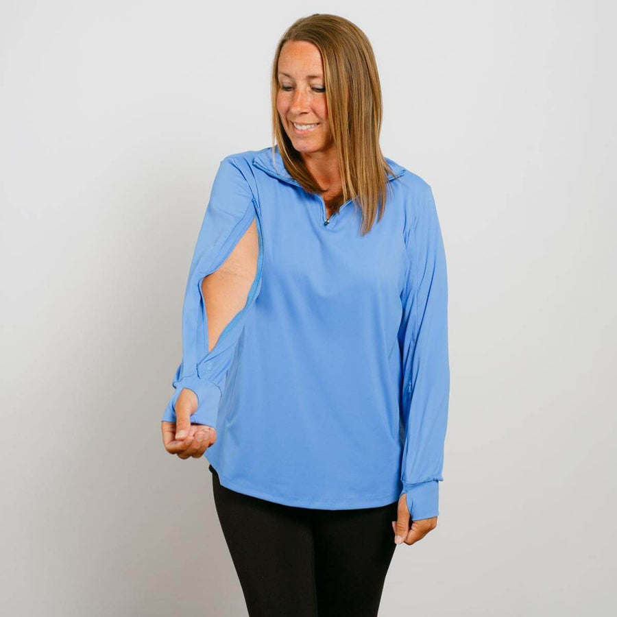 Woman wearing a light blue quarter-zip long-sleeve top with black pants against a white background.