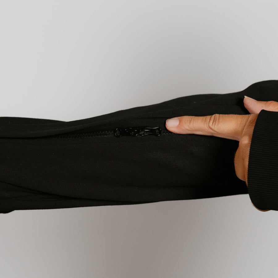Hand pulling down zipper on black zip hoodie against white background.