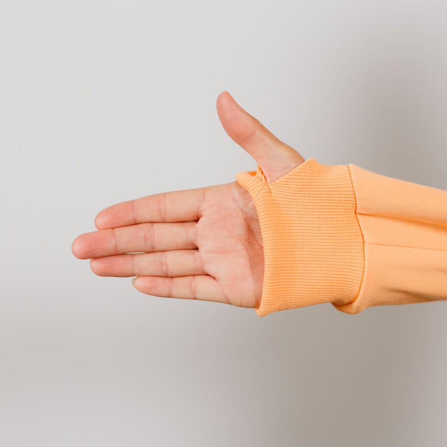 Person wearing peach IV zip hoodie displaying left arm zipper access opening.