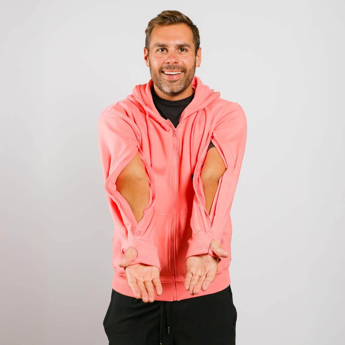 Man wearing a pink hoodie with cut-out sleeves on a plain background | Model is 5'8" 165lbs wearing size M