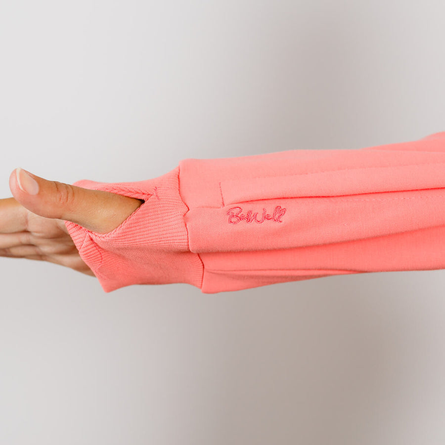 Person wearing coral pink IV zip hoodie with sleeve zipper access open during treatment.