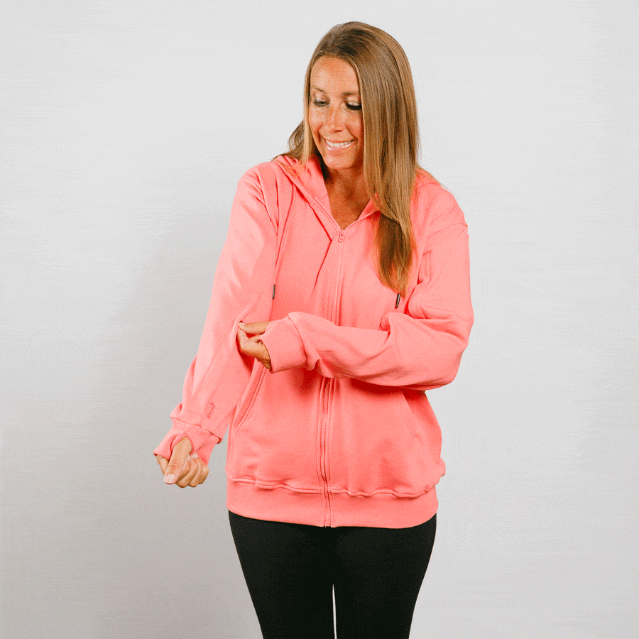 Woman wearing coral pink IV zip hoodie with front zipper, looking down at left sleeve access.