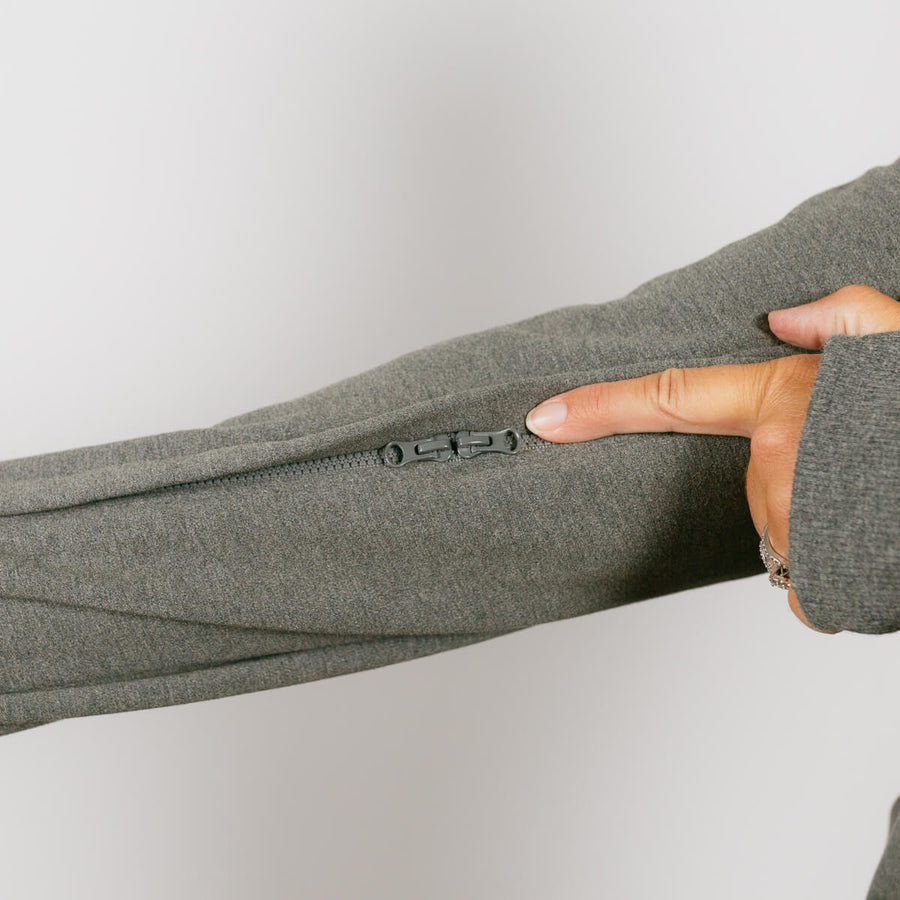 Woman wearing sage green IV zip hoodie demonstrating left sleeve zipper access feature.