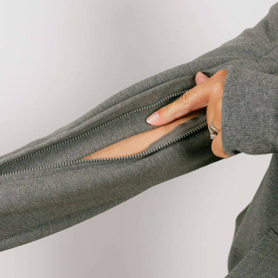 Woman wearing sage green IV zip hoodie with dual sleeve zippers open for medical access.