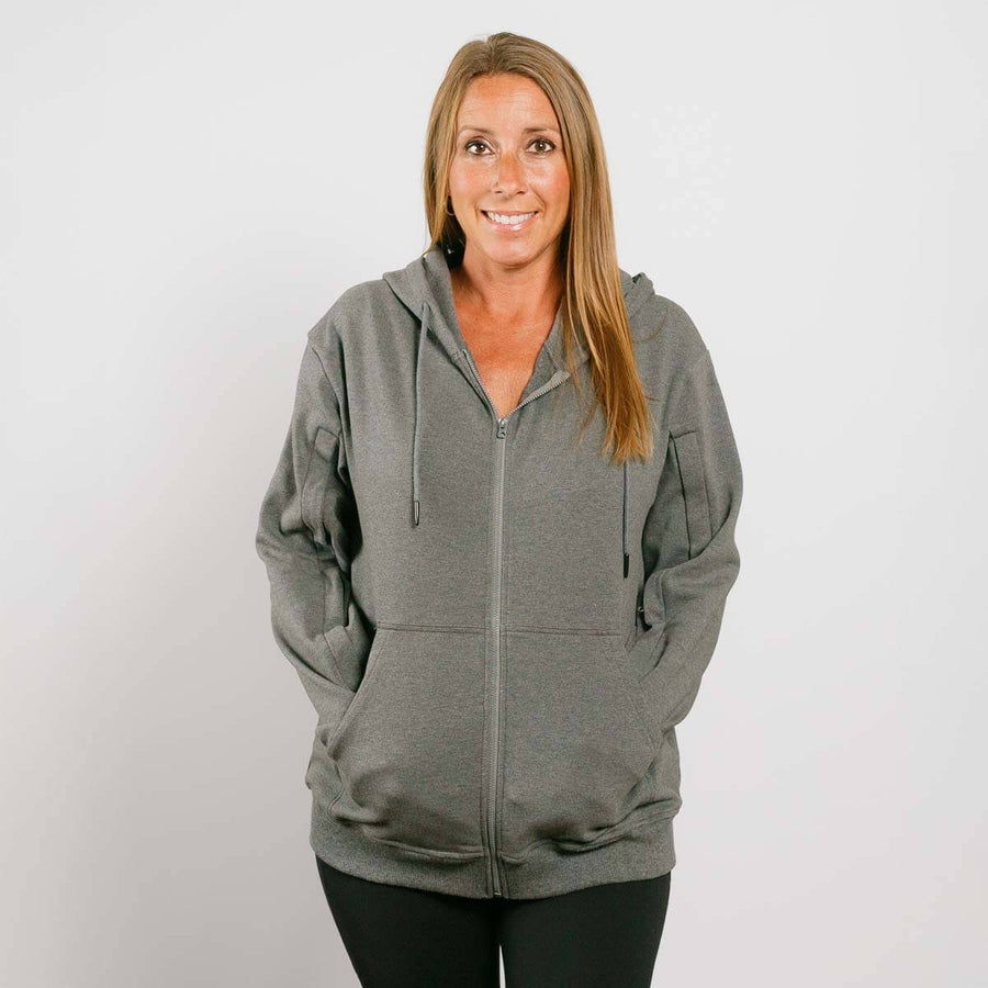 Woman wearing gray zip hoodie with front zipper, standing against white background.