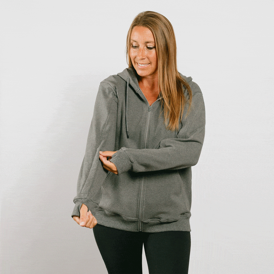 Woman wearing gray zip hoodie with front zipper, looking down at left sleeve access opening.