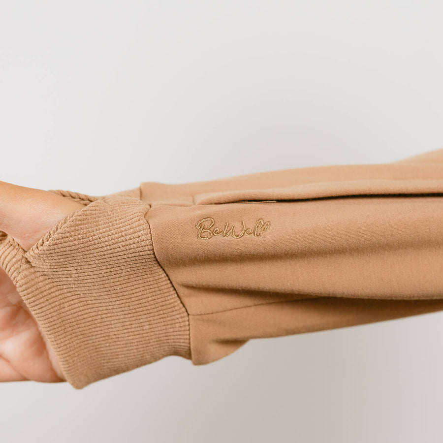Close-up of tan IV zip hoodie sleeve showing ribbed cuff detail and zipper access on arm.