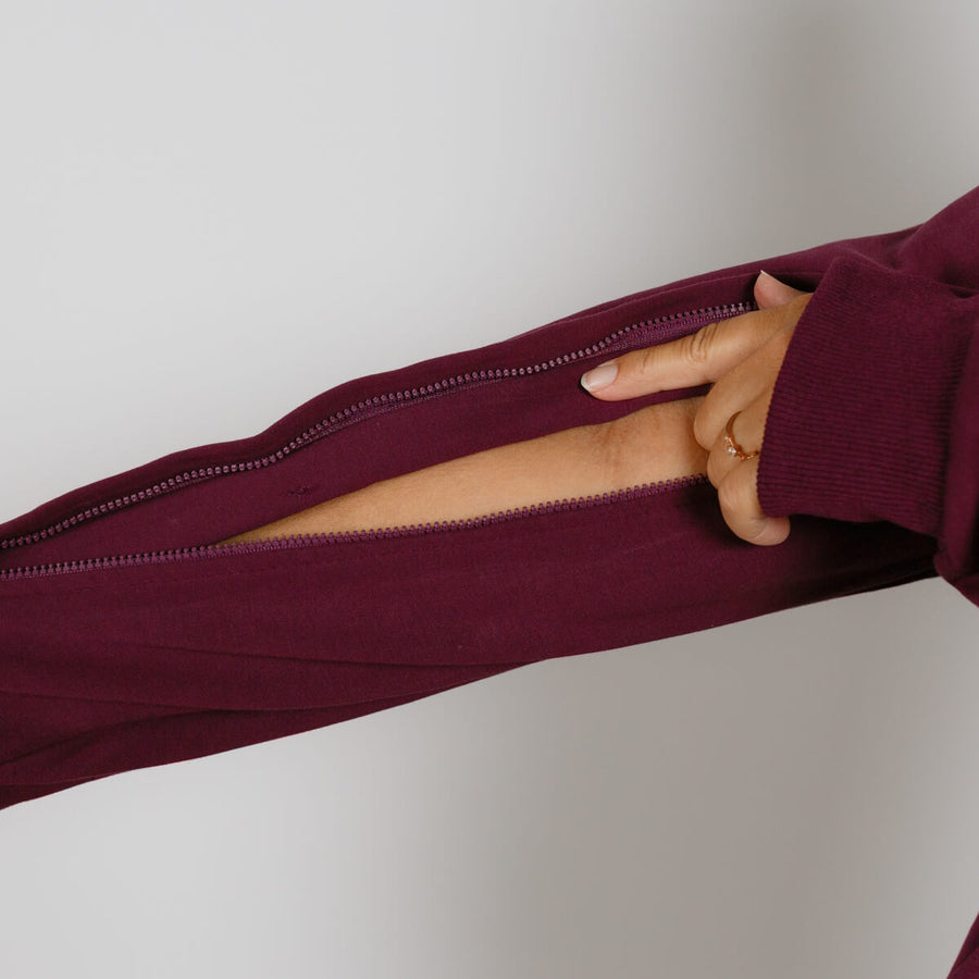 Hand opening the zipper on a burgundy zip hoodie against a white background.