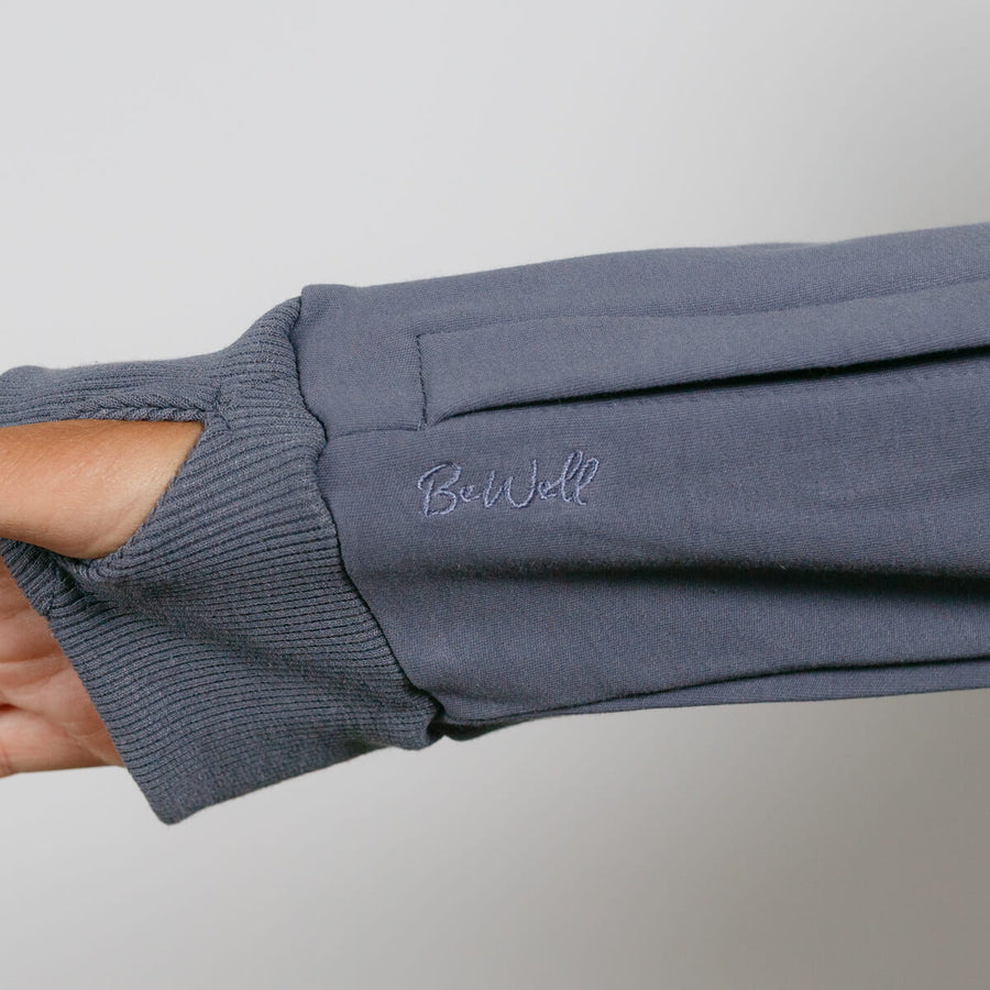 Slate blue zip hoodie with ribbed cuffs worn on a person's arm against a neutral background.