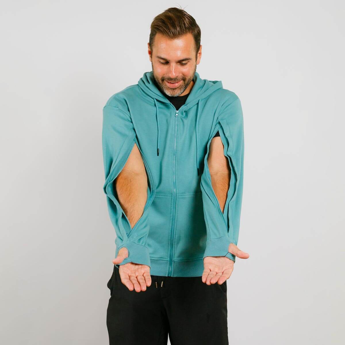 Man wearing turquoise zip-up hoodie with large cutout holes on both sides of torso. | Model is 5'8" 165lbs wearing size M