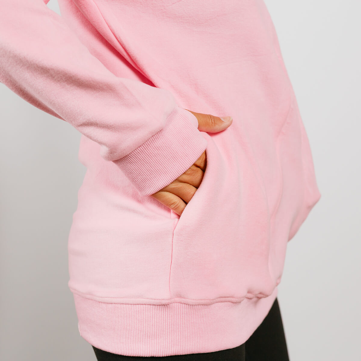 Person wearing pink crewneck sweatshirt with hand in front kangaroo pocket, showing ribbed cuff detail.