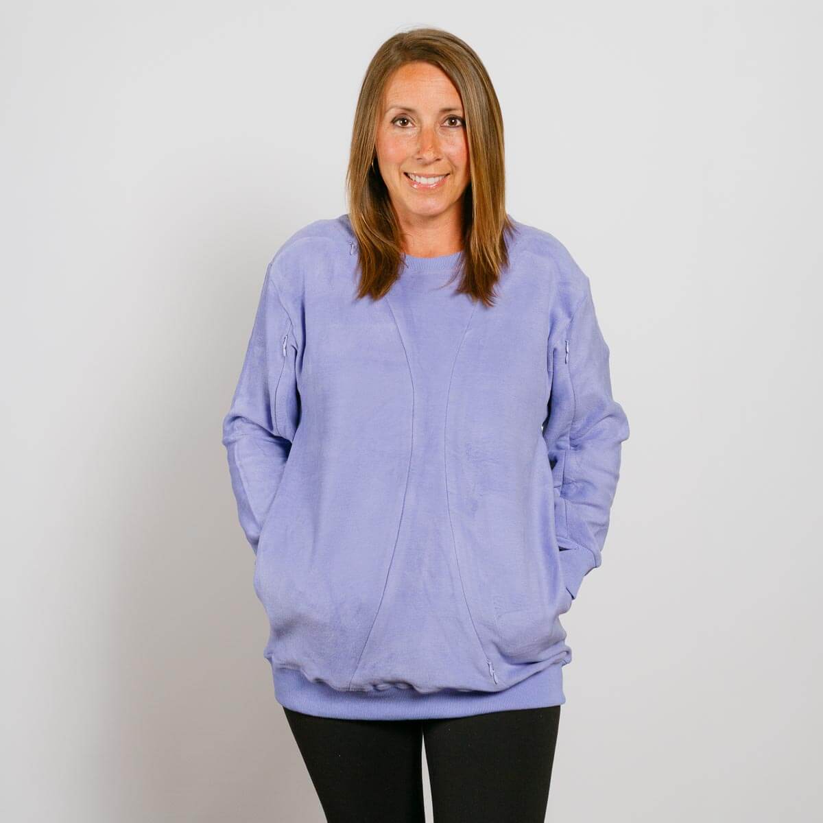 Woman wearing a light purple crewneck sweatshirt with hands in pockets and black pants.