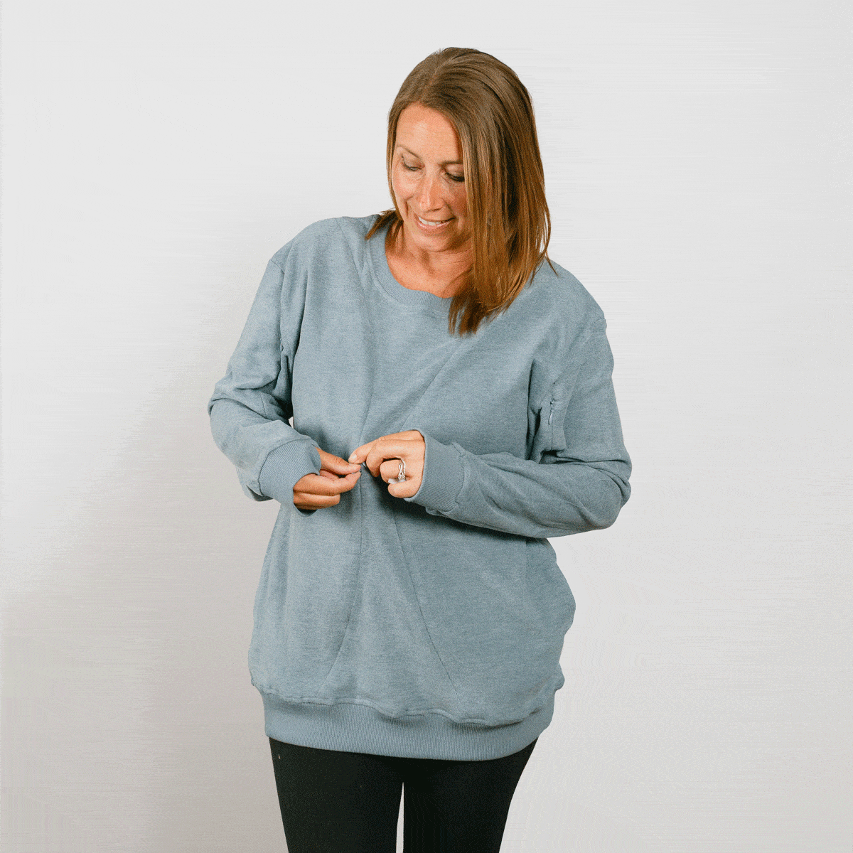 Woman wearing a light blue crewneck sweatshirt over black pants, looking down while adjusting the neckline.