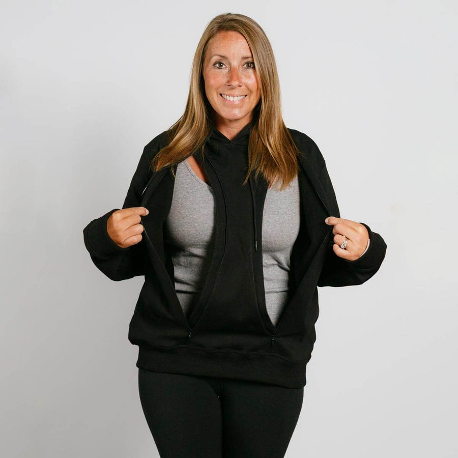 Woman wearing black zip-up hoodie over gray shirt, smiling at camera against white background.