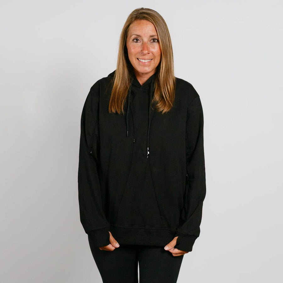 Woman wearing a black hoodie with drawstrings, hands in front pockets, smiling at camera.