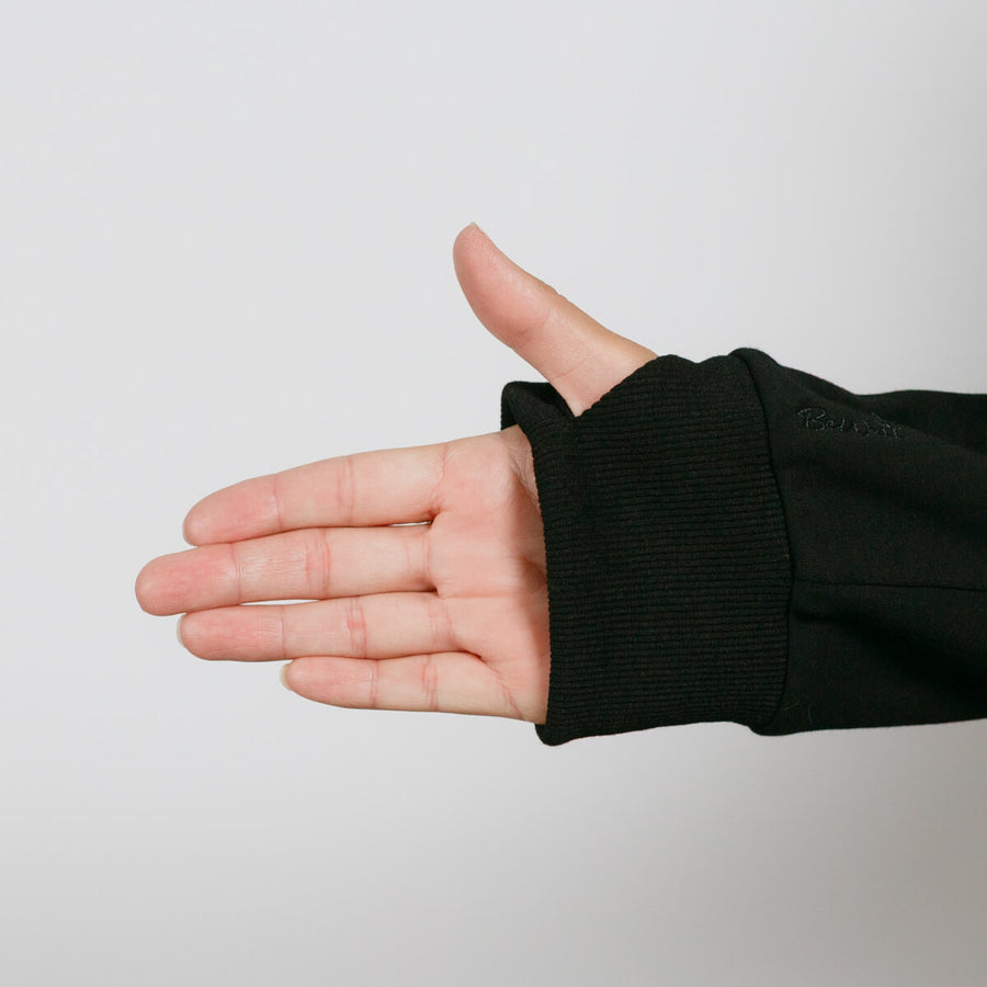 Open palm hand wearing black ribbed sleeve cuff against neutral gray background.