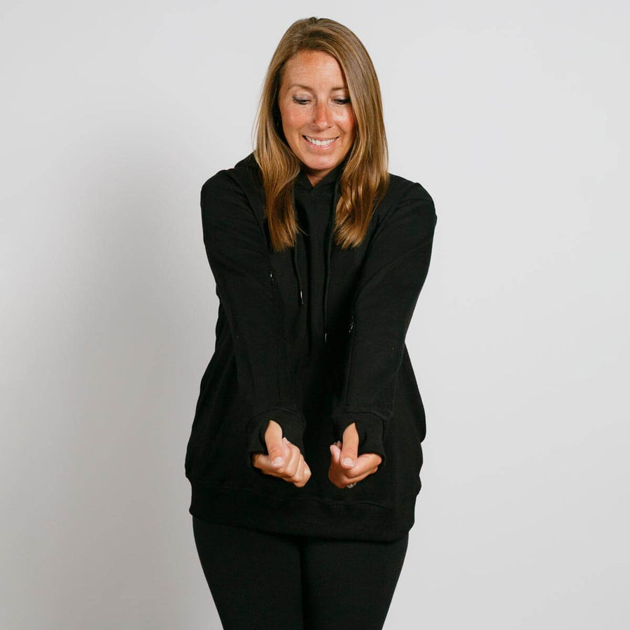 Woman wearing black hoodie and matching pants, smiling with hands gesturing outward.
