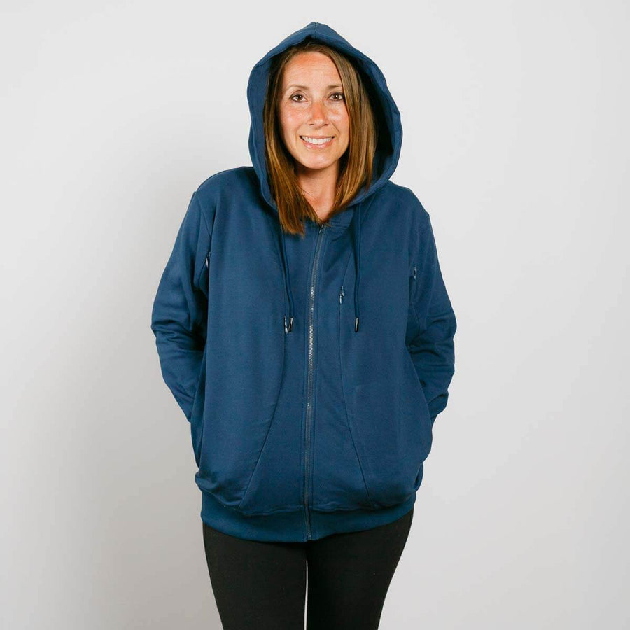 Woman wearing a navy blue zip-up hoodie with hands in pockets, smiling at camera.
