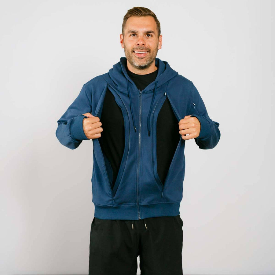 Man wearing a dark blue hoodie opening both sides of the front via zip up holes with a plain background