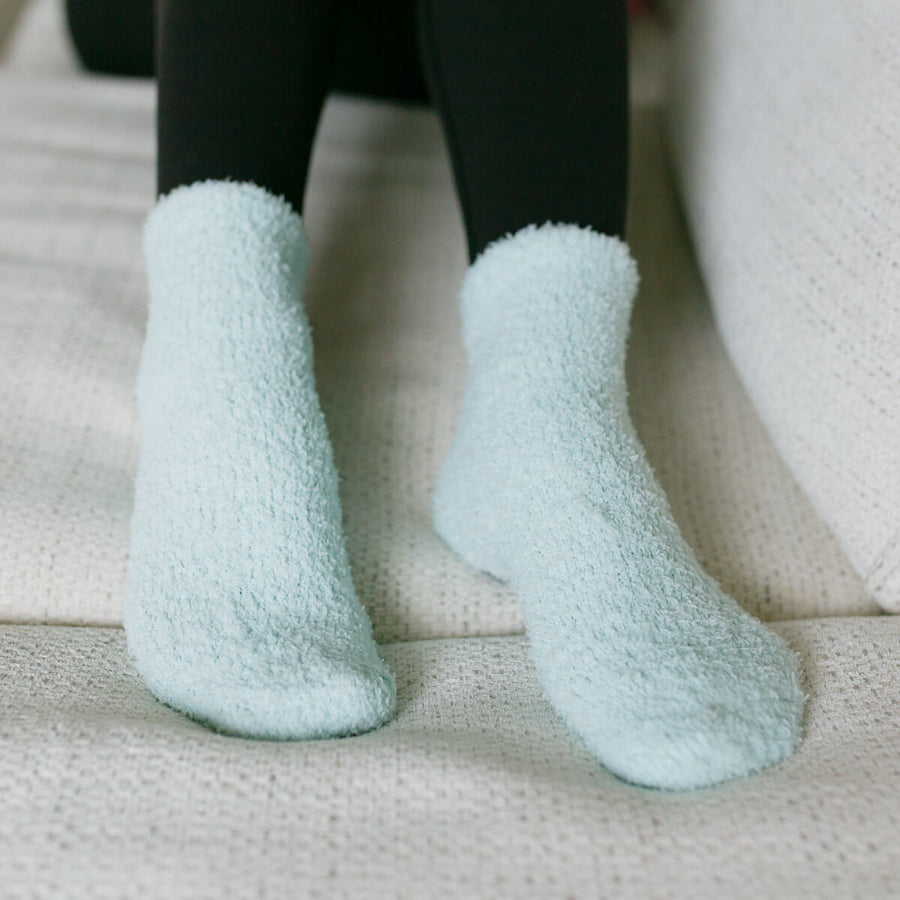 Person wearing light blue fuzzy rest day socks, close-up detail view.