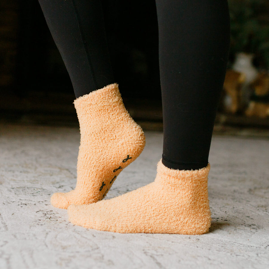 Person wearing peach fuzzy Rest Day Socks with black leggings, close-up side view.