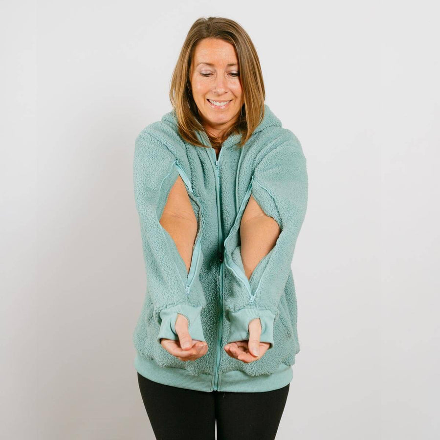 Woman wearing sage green sherpa zip hoodie with arm access openings, front view.