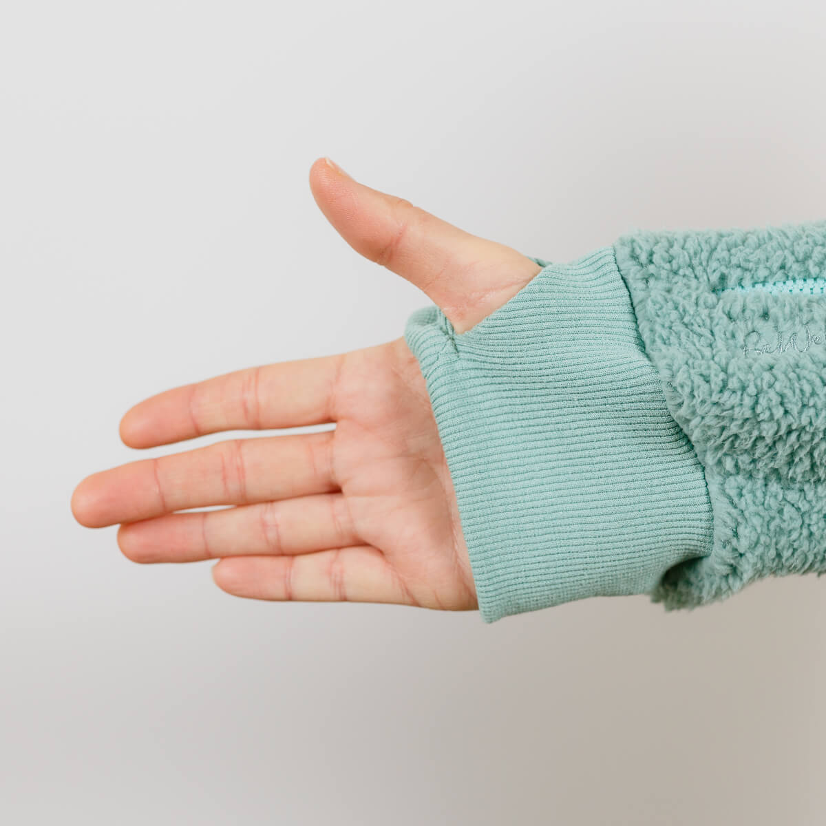 Close-up of child's hand wearing sage green sherpa hoodie with ribbed cuff detail.