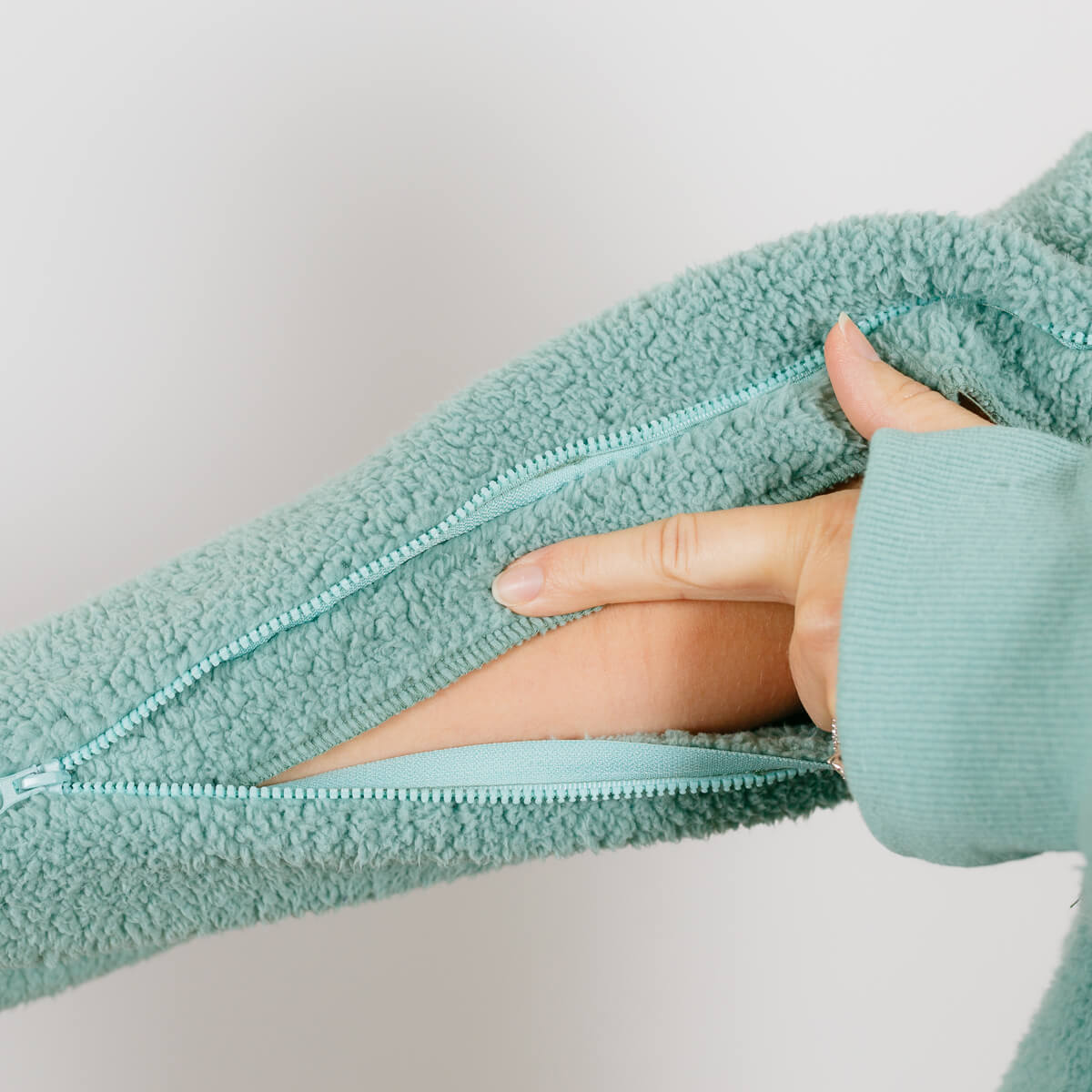 Close-up of sage green sherpa hoodie showing open side zipper and arm access detail.