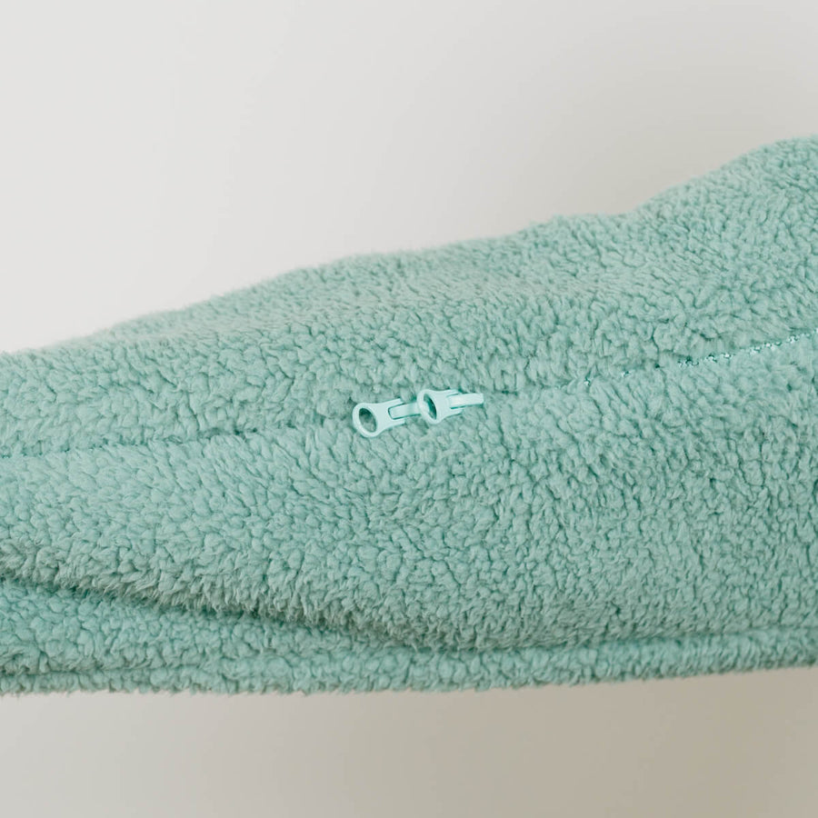 seafoam color sherpa fabric shows a white zipper pull detail against textured fleece material.
