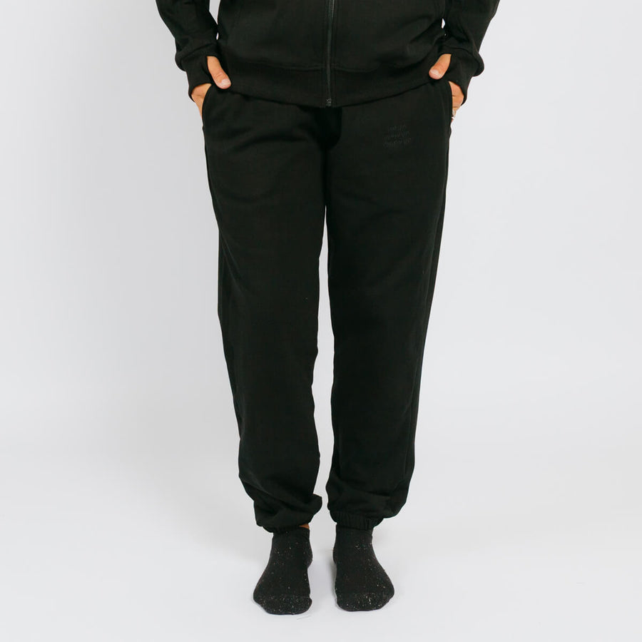 Black jogger sweatpants with cuffed ankles on a model wearing a matching black zip-up hoodie.