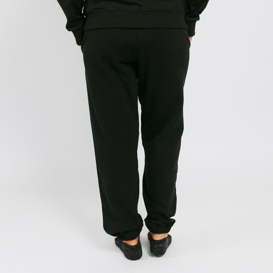 Person wearing black sweatpants standing against white background, viewed from behind.