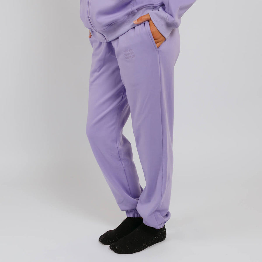 Person wearing lavender sweatpants with orange drawstring details and black socks against white background.