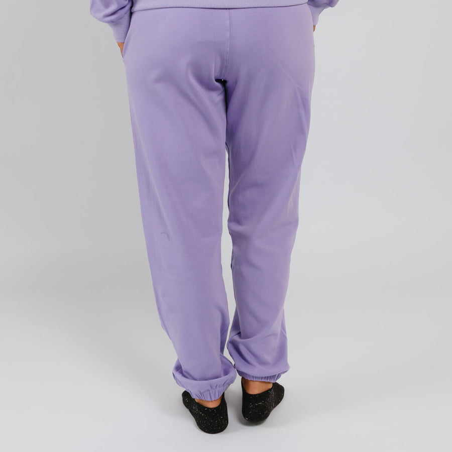 Person wearing lavender purple sweatpants with cuffed ankles, viewed from behind.