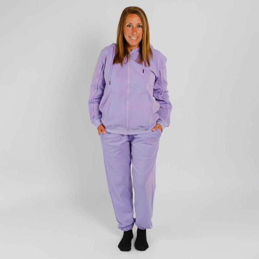 Woman wearing a lavender zip-up hoodie and matching sweatpants with black socks.