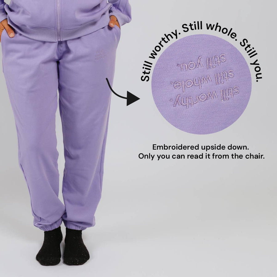 Purple sweatpants with embroidered text on the back thigh, readable only when seated.